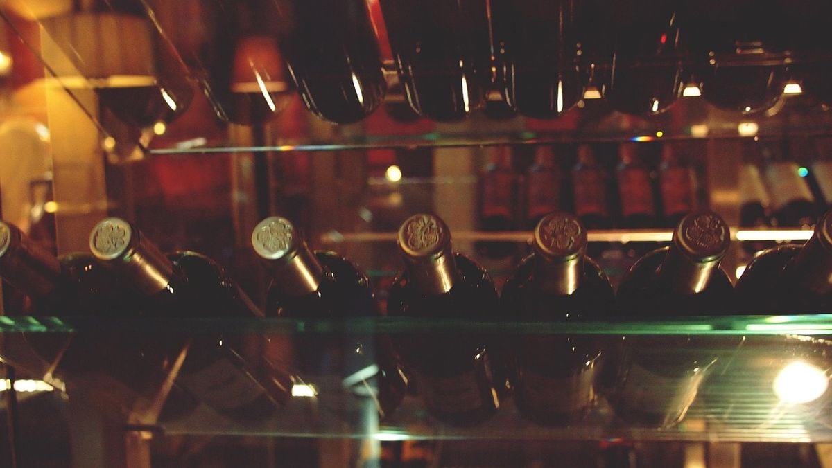 Garrafas de vinho deitadas atras da porta de vidro de uma adega climatizada