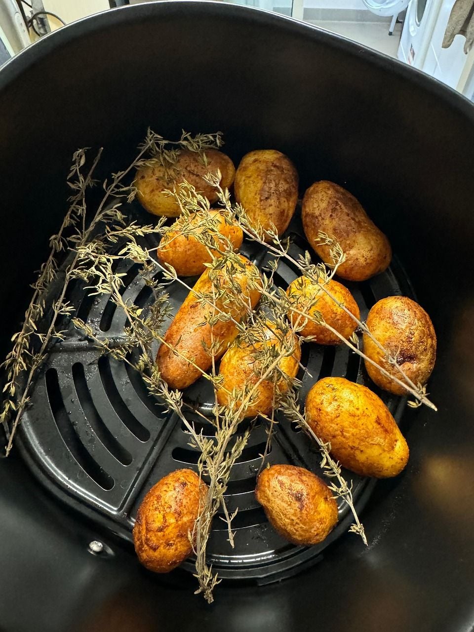 Batatas temperadas com ervas assando dentro do cesto de uma air fryer