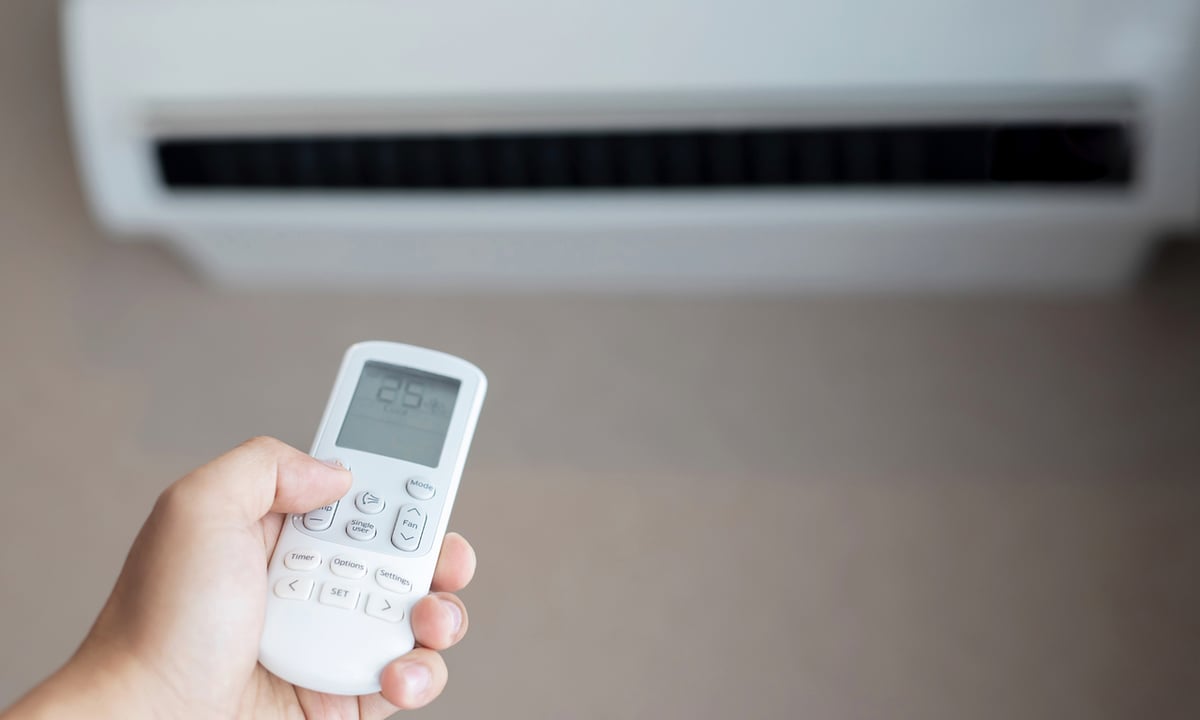 Controle remoto de ar-condicionado split de parede Mão segurando controle remoto na frente de um ar-condicionado split